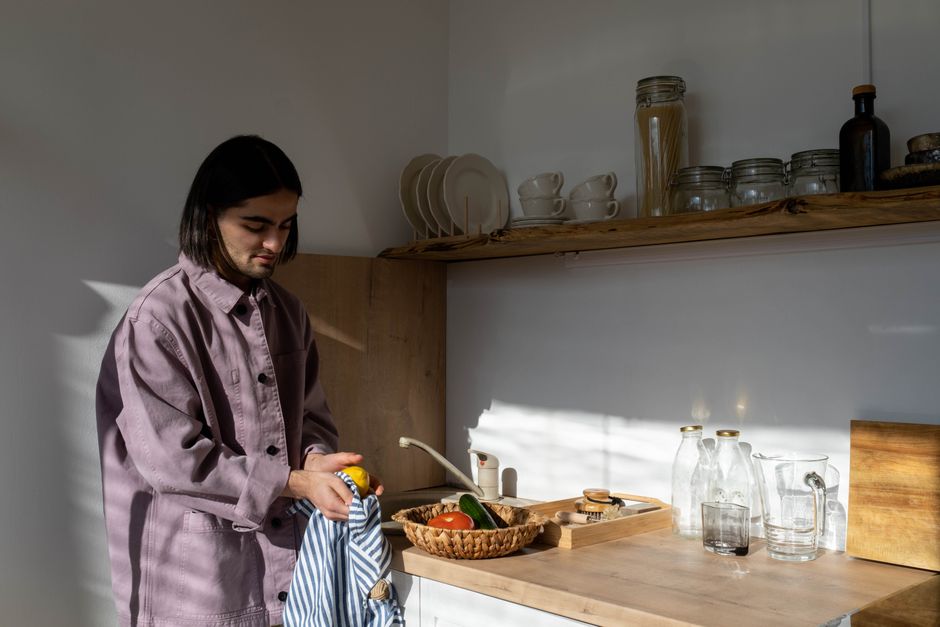 A man stands in a minimalist kitchen, preparing vegetables on a sunny day.
