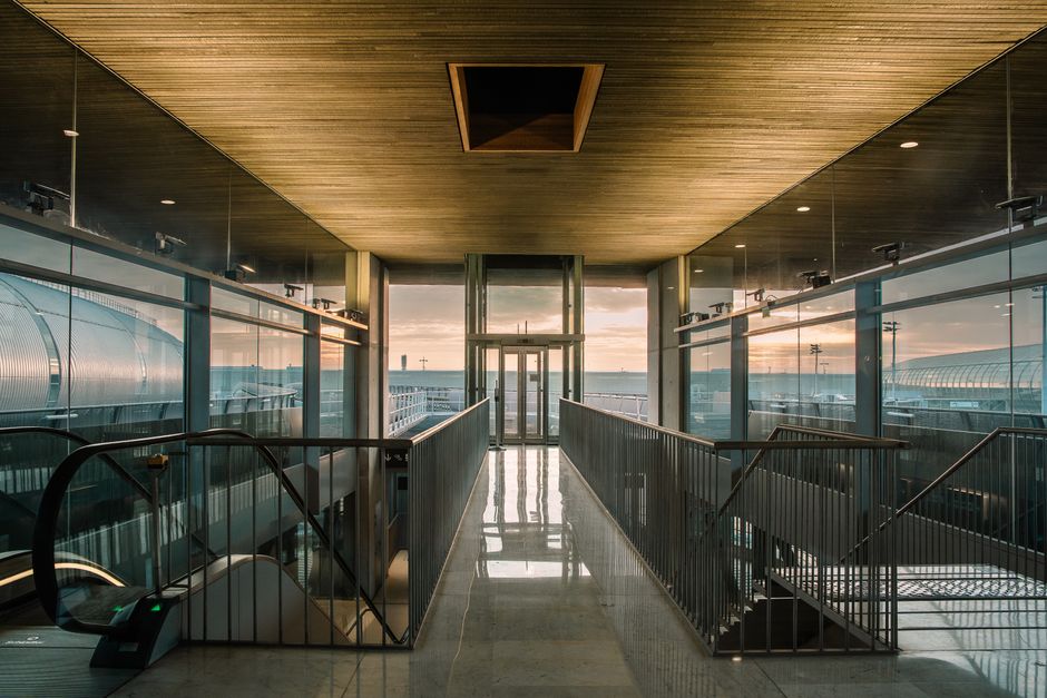 A modern airport terminal corridor with glass walls, overlooking the outdoor area at sunri