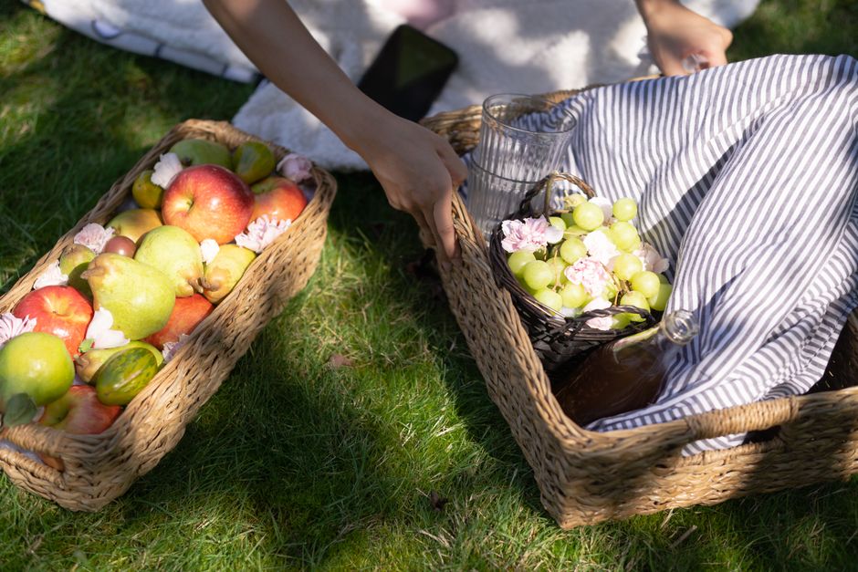 A vibrant summer picnic featuring fresh apples, pears, and grapes in woven baskets on a gr