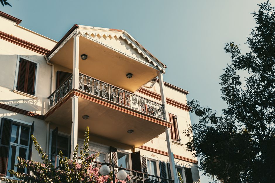 Elegant colonial-style home with balcony under a clear blue sky, surrounded by greenery.