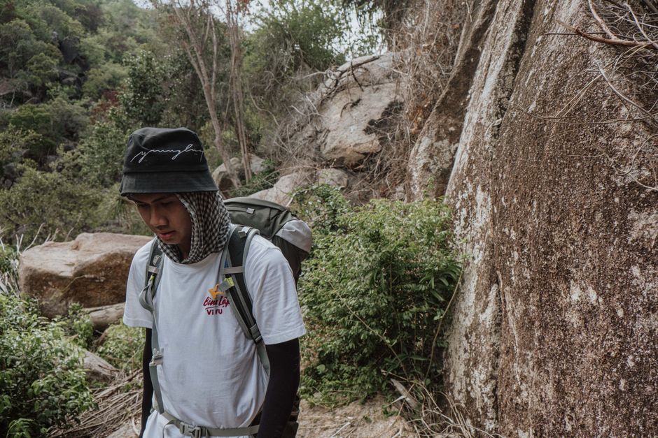 Teenager hiking through a rocky and lush landscape, wearing a backpack and hat, embodying adventure.