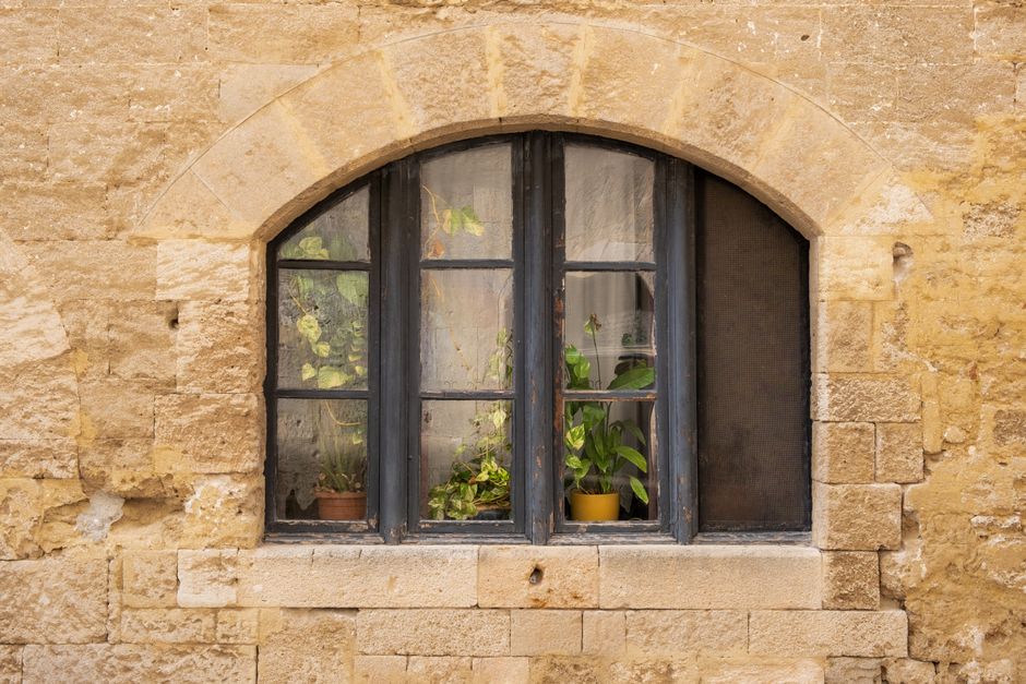 Charming weathered stone window with potted plants in Rhodes, Greece.