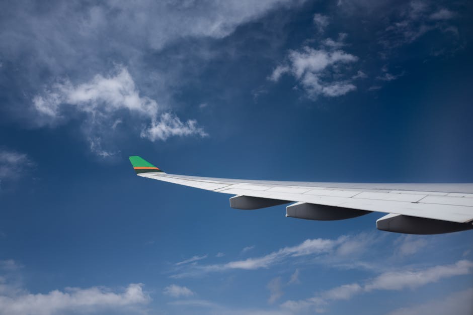 View of an airplane wing soaring through a clear blue sky with white clouds.