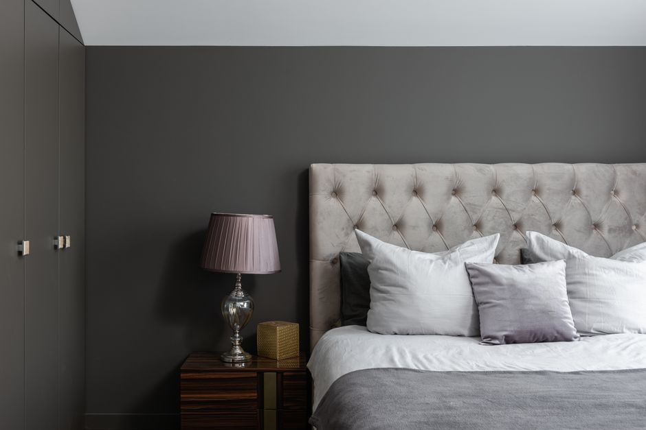 Comfortable bed with soft cushions placed near lamp on bedside table in stylish bedroom wi