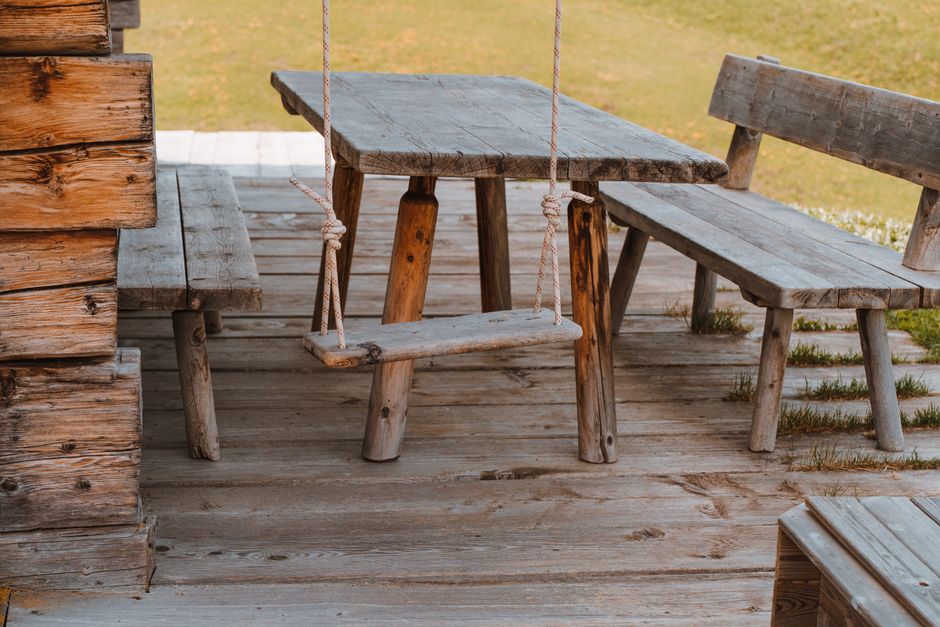 A rustic wooden bench and swing set on a sunny patio in Sankt Ulrich, Italy.