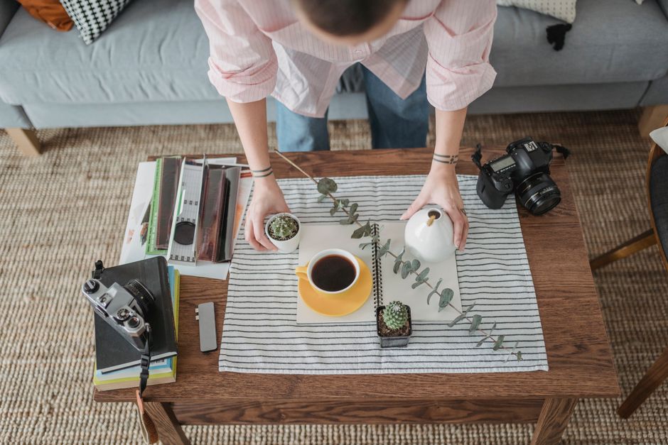 From above of crop unrecognizable photographer arranging green plants on wooden table with