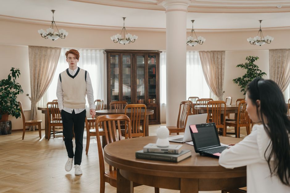 A serene library space with students studying and a man walking, capturing a focused academic environment.