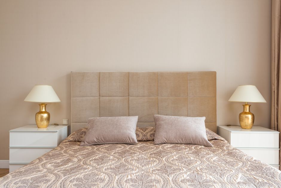 Interior of bedroom with big bed with soft headboard and lamps placed on nightstands in daylight