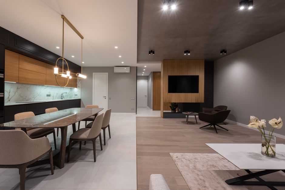 Modern apartment interior with dining table and chairs under pendant lamp next to open kit