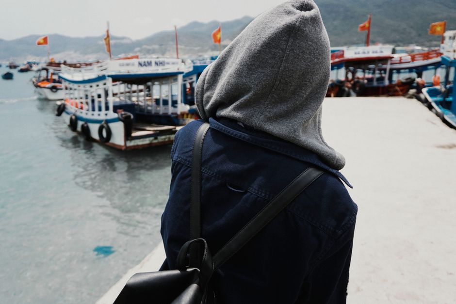Back view of a tourist in a grey hood admiring boats on a lakeside dock.
