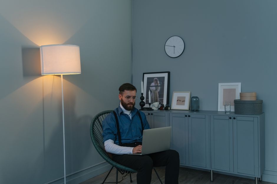 Adult man in blue shirt sitting on a chair with a laptop in a modern home office setting.