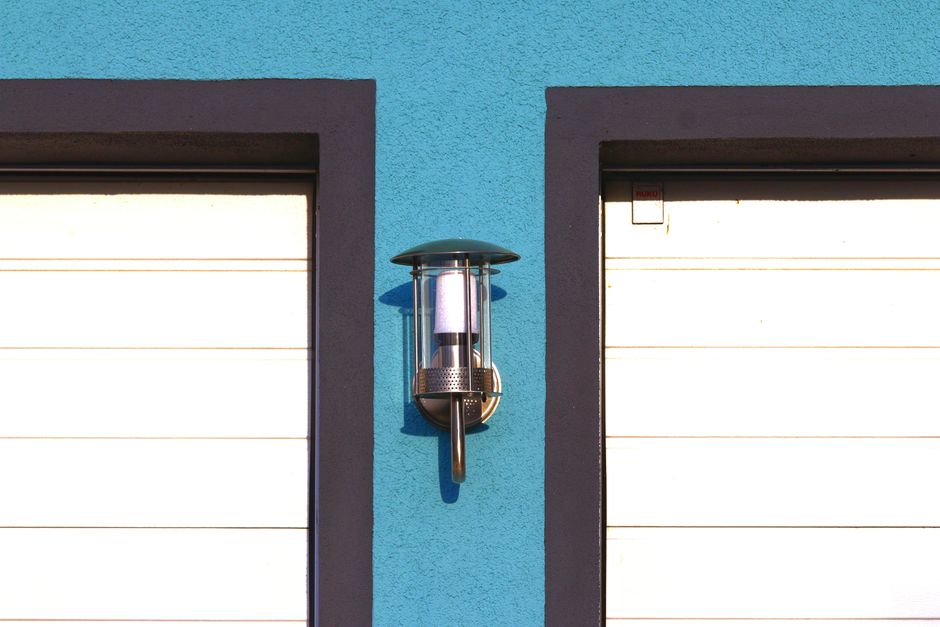 Modern outdoor wall light fixture on vibrant blue facade with contrasting black and white elements.