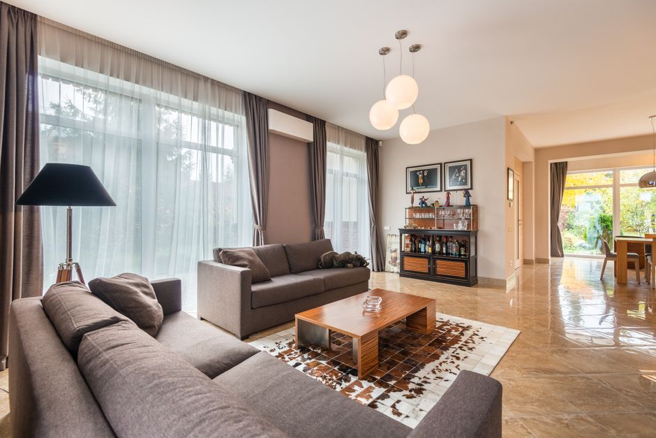 Interior of contemporary spacious living room with comfortable sofa and wooden table near windows with curtains