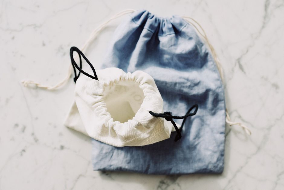Top view of white and blue fabric eco friendly bags with drawstrings placed nearby on whit
