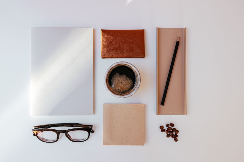 A minimalist flatlay with coffee, glasses, and office supplies on a white background.