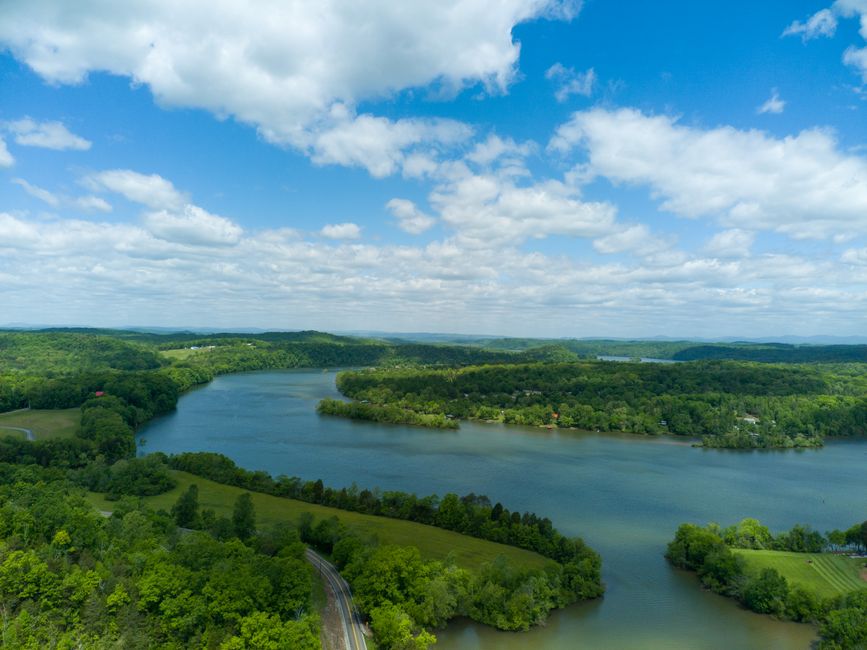 A peaceful aerial view of a scenic river surrounded by lush greenery under a clear blue sky.