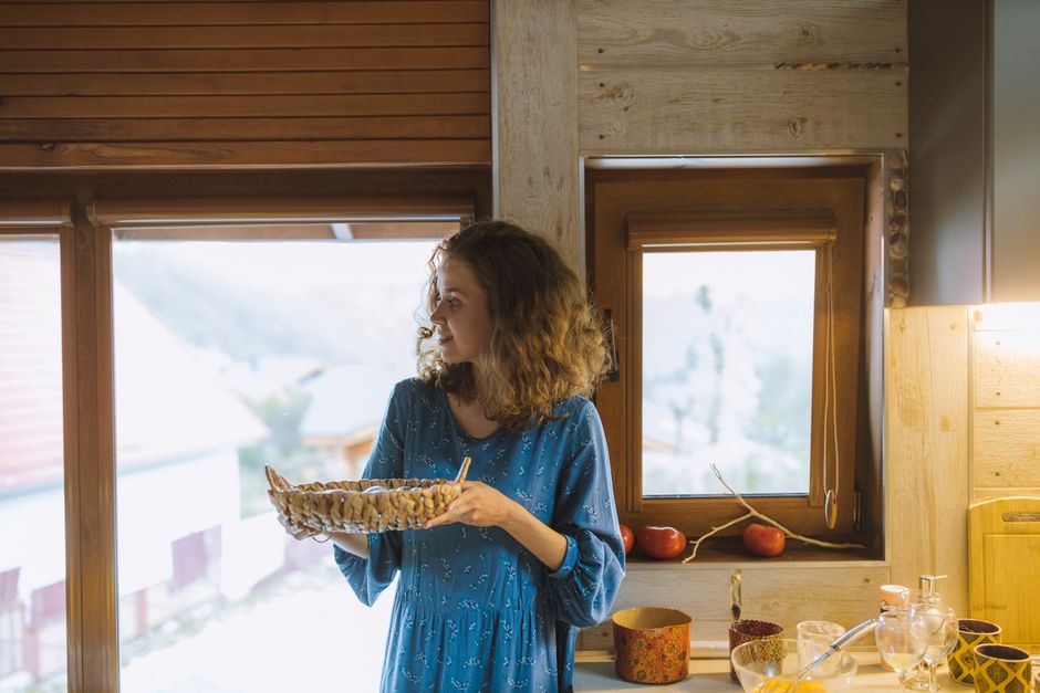 Woman in a blue dress holding a woven basket in a cozy kitchen setting with natural light 